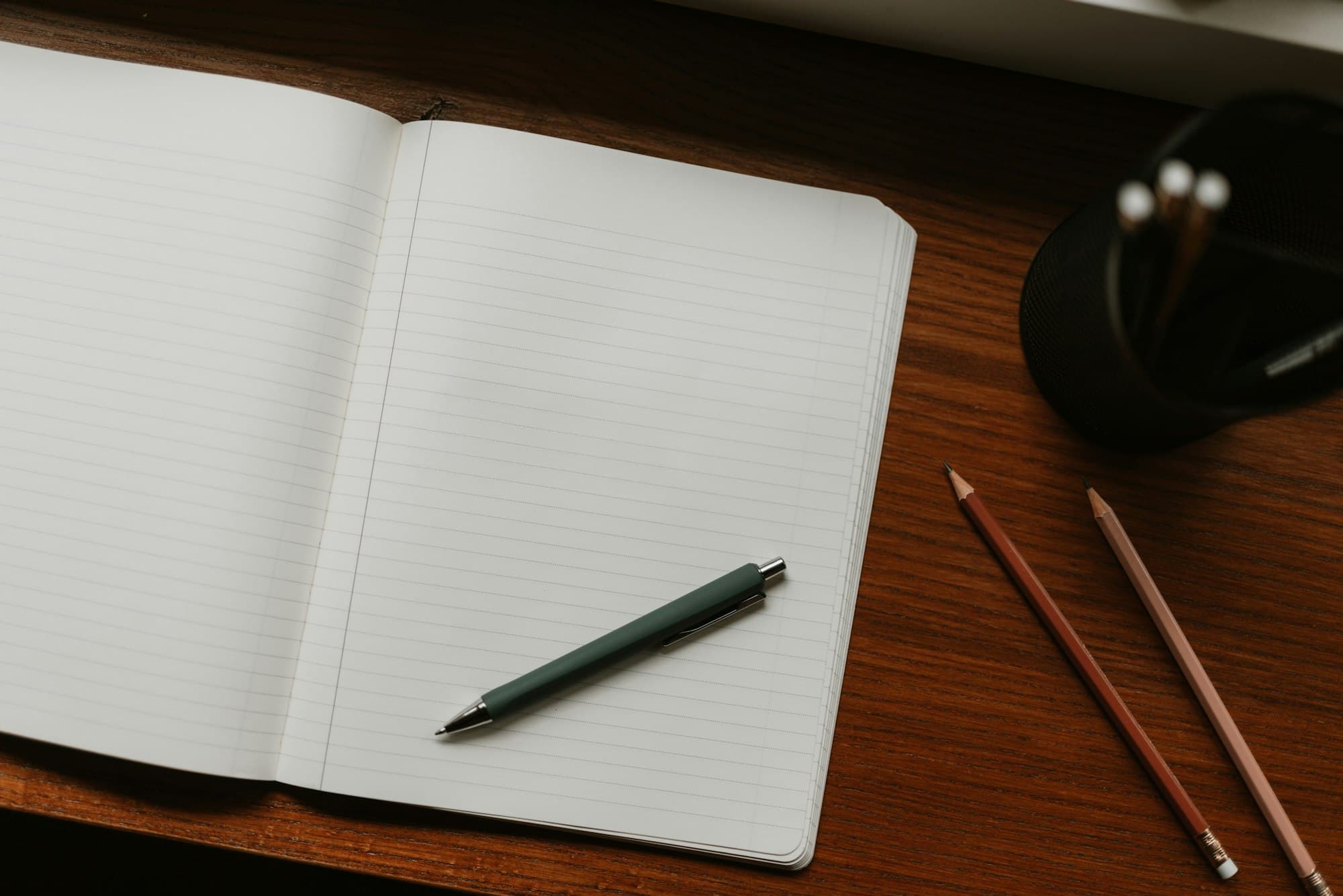 An open notebook with a pen and pencils resting on a warm wooden desk, soft morning light.